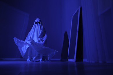 Photo of Creepy ghost. Woman covered with sheet in blue light, low angle view