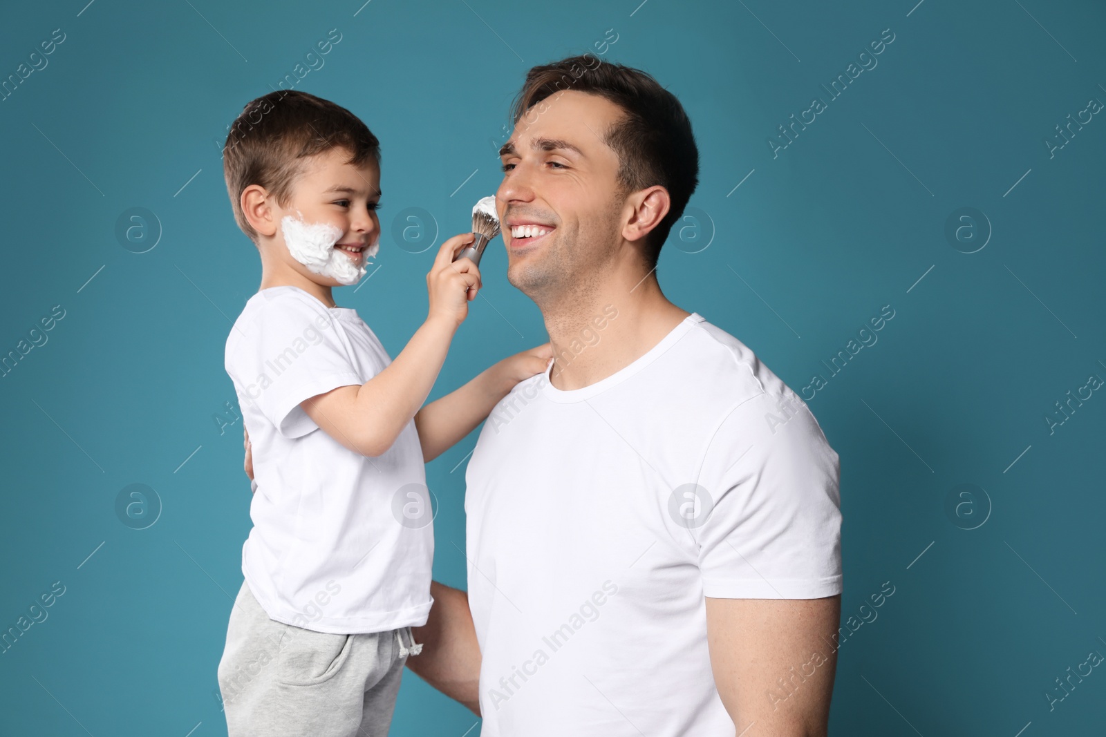 Photo of Son applying shaving foam onto dad's face against color background