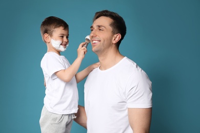 Son applying shaving foam onto dad's face against color background