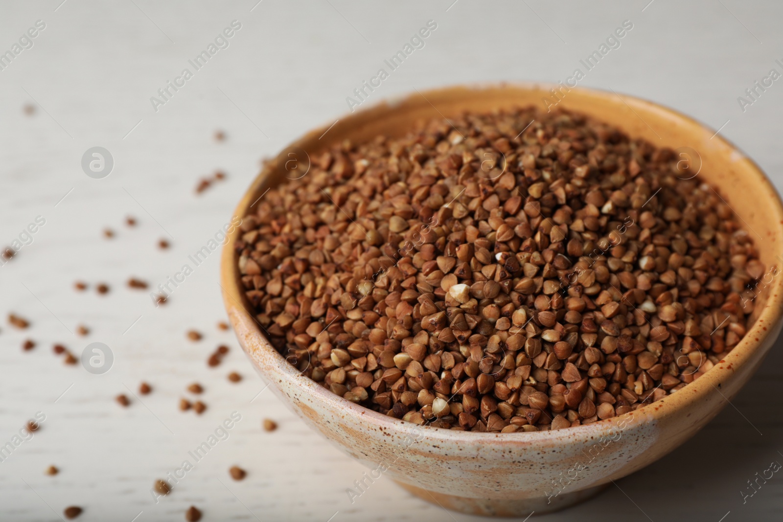 Photo of Uncooked buckwheat in ceramic bowl on table