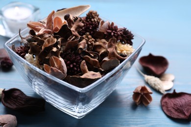 Aromatic potpourri of dried flowers in glass bowl on light blue wooden table, closeup