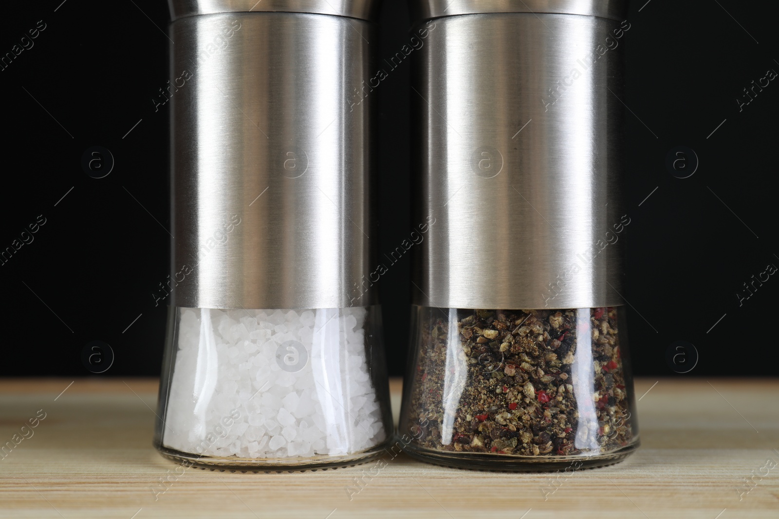 Photo of Salt and pepper shakers on light wooden table against black background, closeup