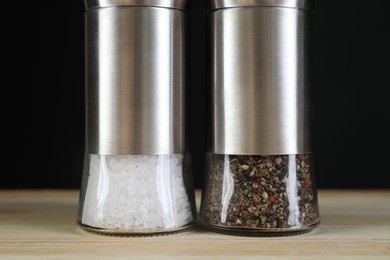 Photo of Salt and pepper shakers on light wooden table against black background, closeup