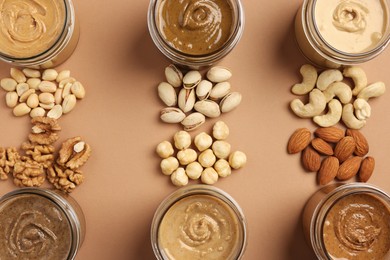 Photo of Many tasty nut butters in jars and nuts on beige table, flat lay
