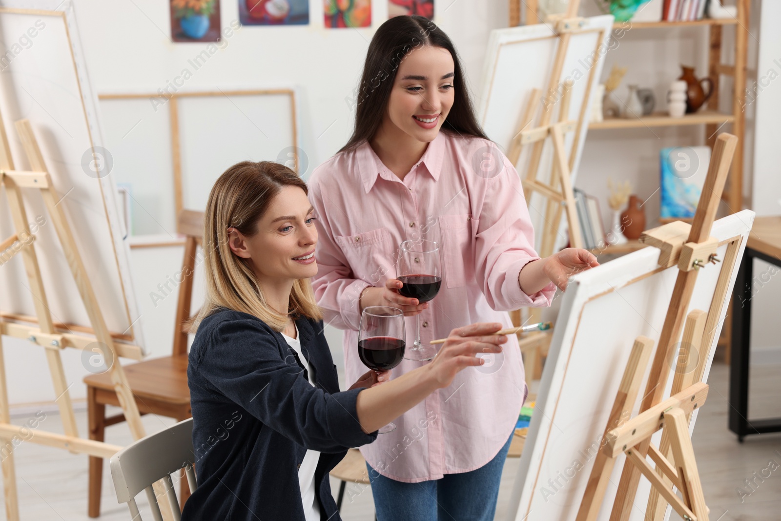 Photo of Artist and her student with glasses of wine having painting class in studio. Creative hobby