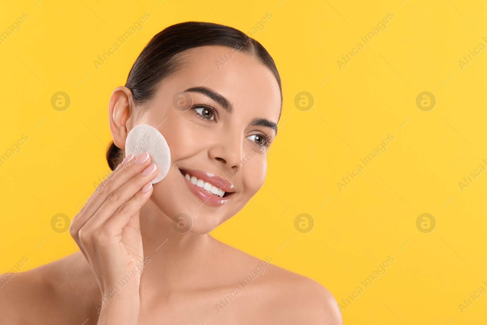 Photo of Beautiful woman removing makeup with cotton pad on yellow background. Space for text