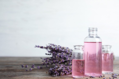 Photo of Bottles with aromatic lavender oil on wooden table. Space for text