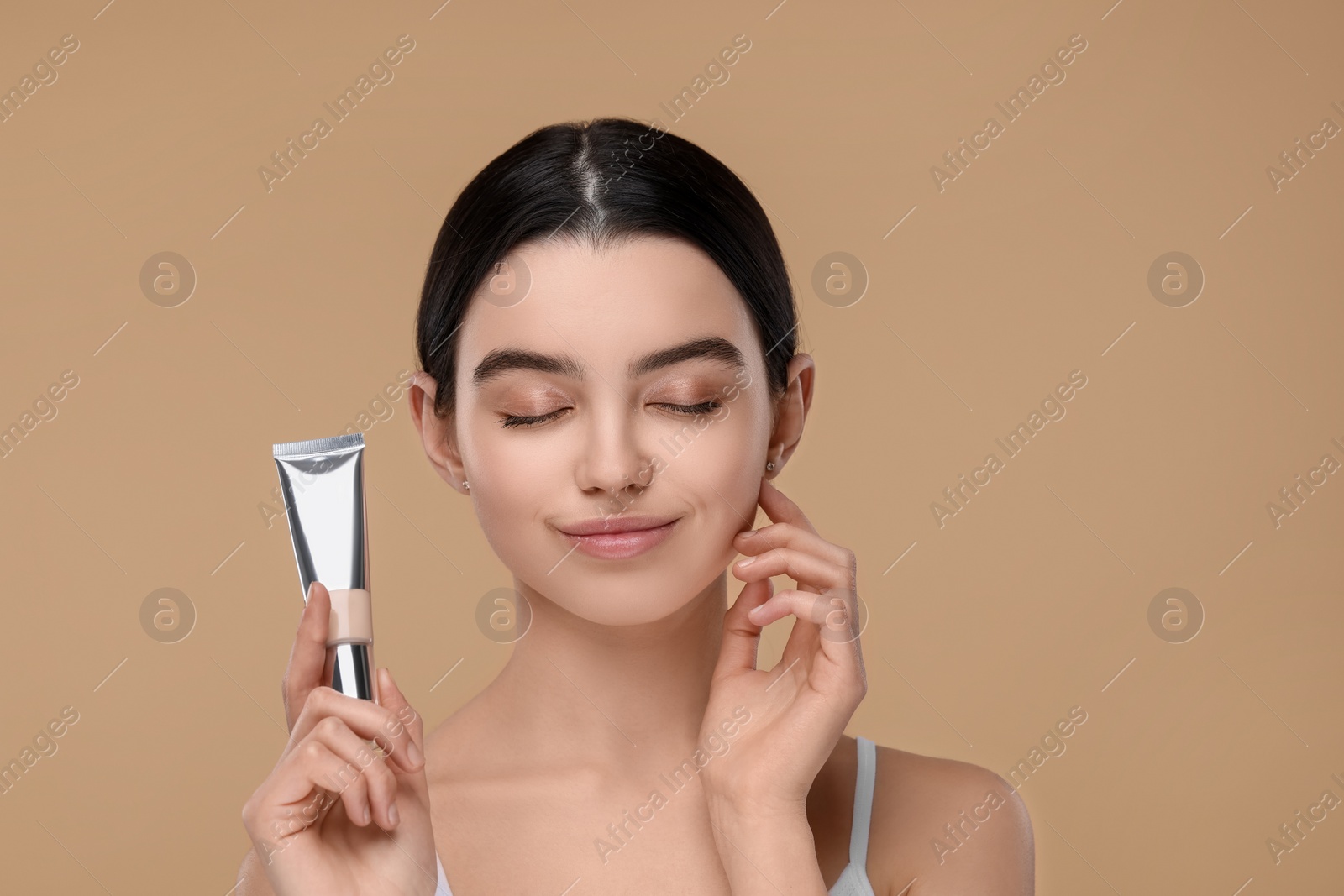 Photo of Teenage girl holding tube with foundation on beige background