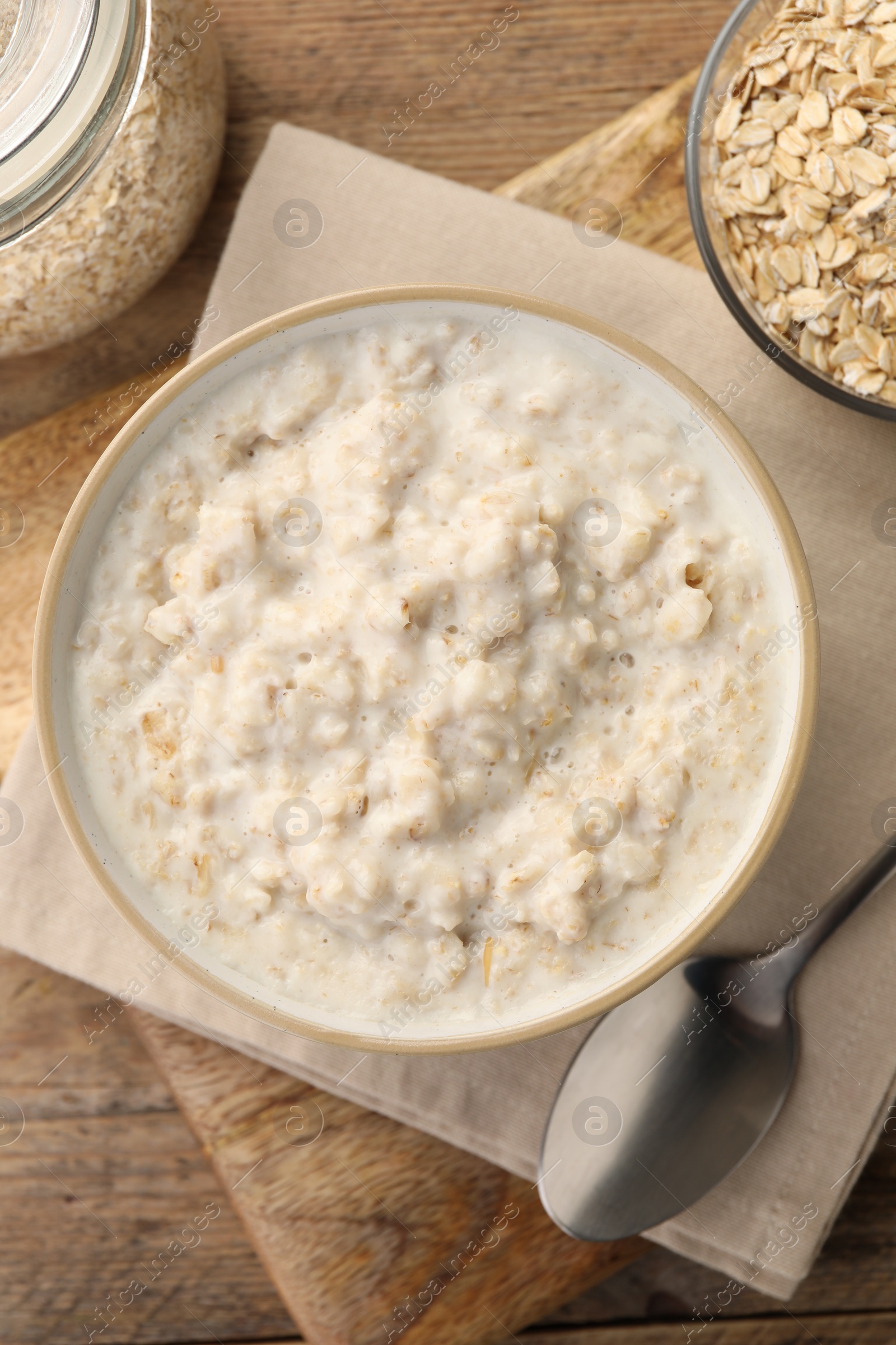 Photo of Tasty boiled oatmeal in bowl, flakes and spoon on wooden table, flat lay