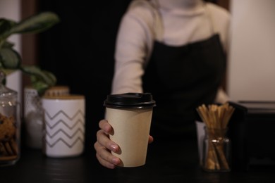 Barista putting takeaway coffee cup on table indoors, closeup
