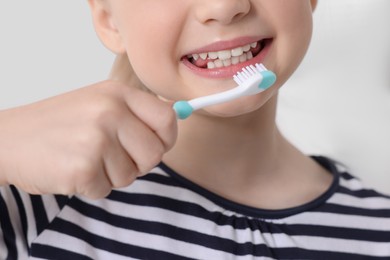 Photo of Little girl brushing her teeth with plastic toothbrush indoors, closeup