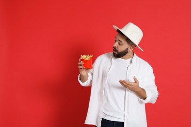 Photo of Emotional young man with French fries on red background, space for text