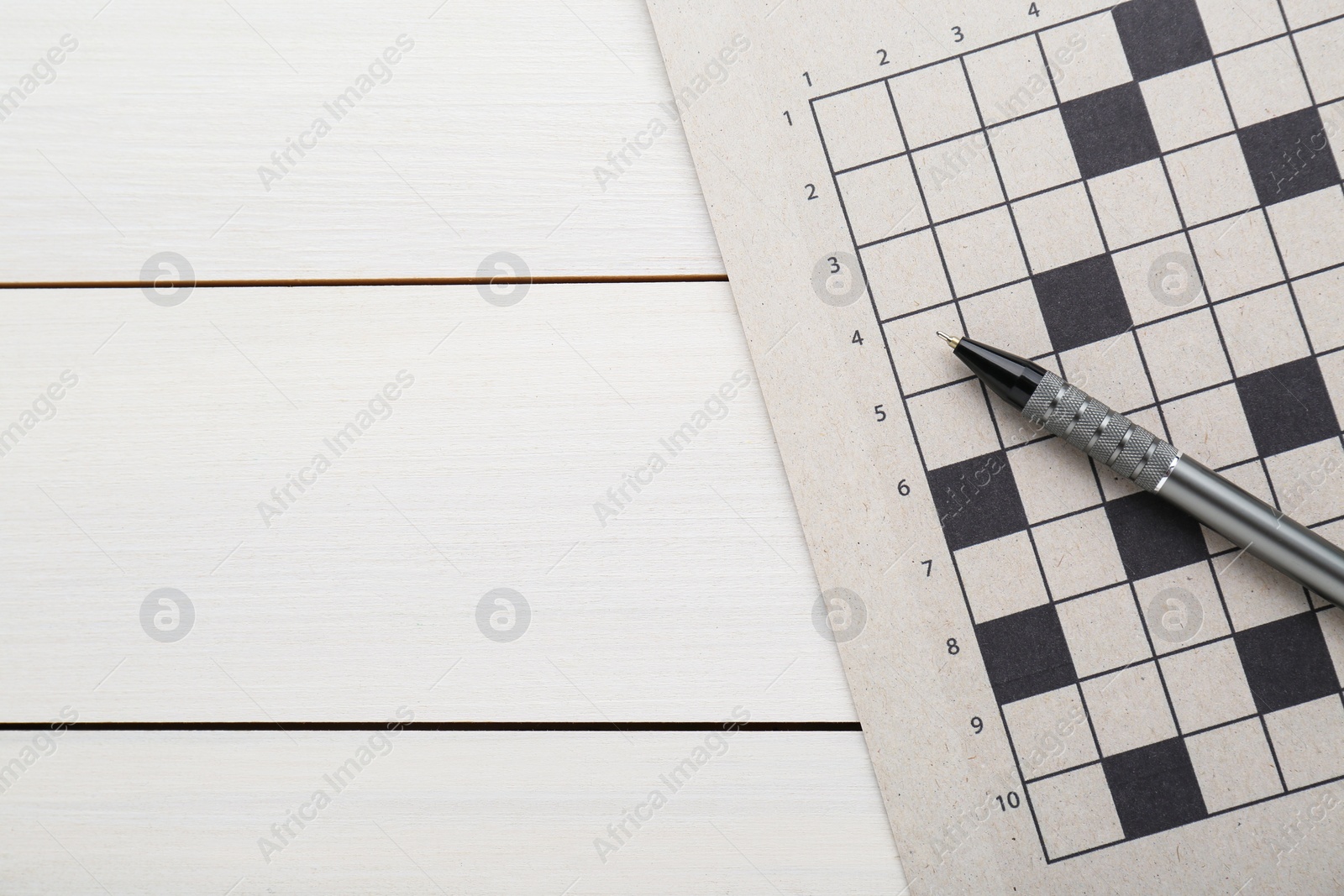 Photo of Blank crossword and pen on white wooden table, top view. Space for text