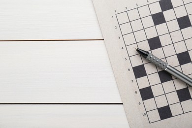 Photo of Blank crossword and pen on white wooden table, top view. Space for text