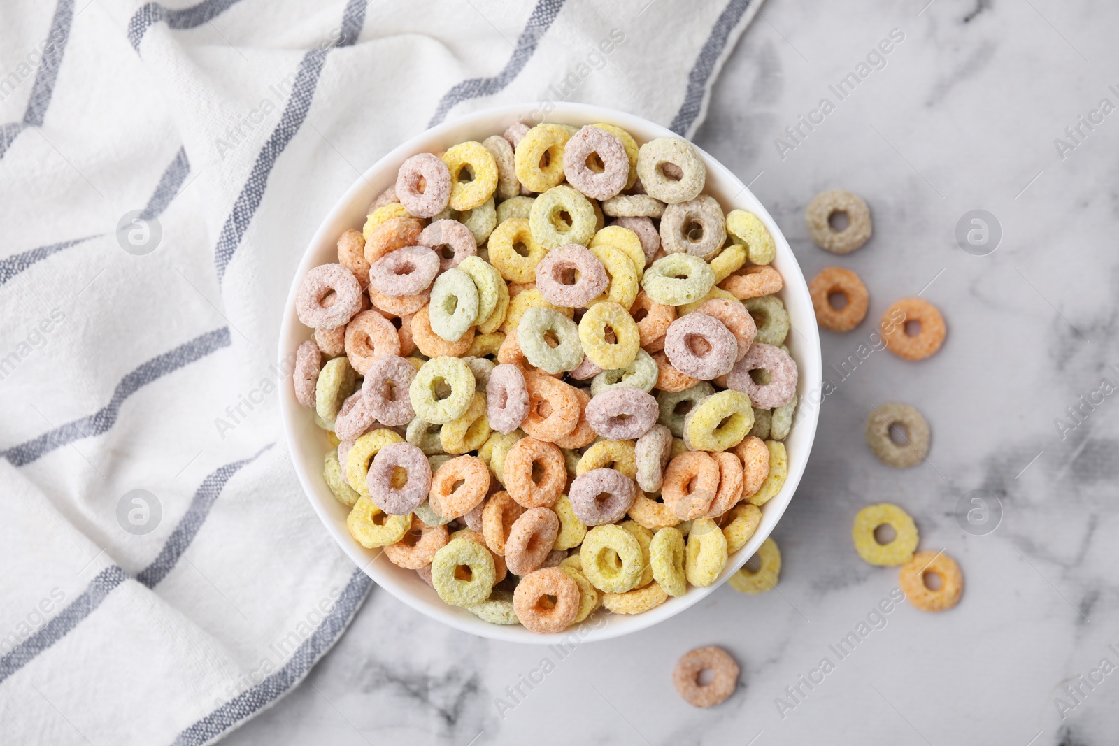 Photo of Tasty cereal rings in bowl on white marble table, top view