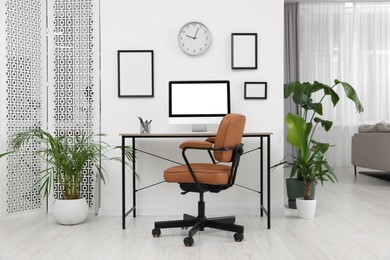 Stylish room interior with comfortable office chair, desk and houseplants