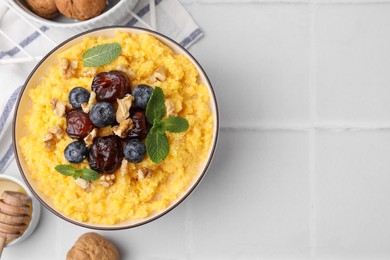 Photo of Tasty cornmeal with blueberries, dates, walnuts and honey in bowl on white table, flat lay. Space for text