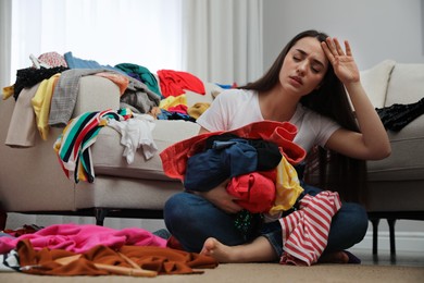 Photo of Tired young woman with lots of clothes in room. Fast fashion