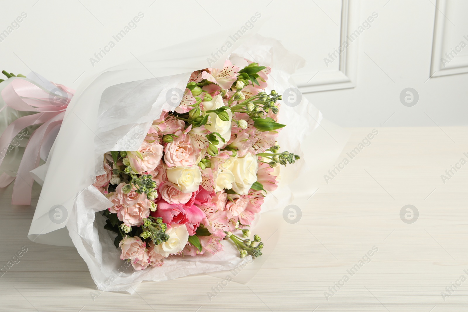 Photo of Beautiful bouquet of fresh flowers on wooden table near white wall, space for text