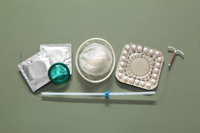 Photo of Contraceptive pills, condoms and intrauterine device on olive background, flat lay. Different birth control methods