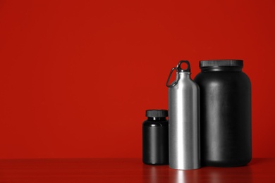 Photo of Black jars with protein powder and bottle on table against red background. Space for text