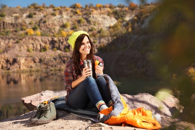 Female camper with thermos sitting on sleeping bag in wilderness