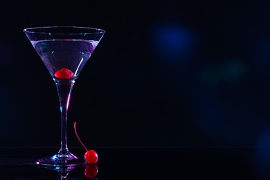 Glass with martini and cherry on black background, space for text