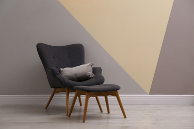 Photo of Comfortable armchair with cushion and footstool indoors