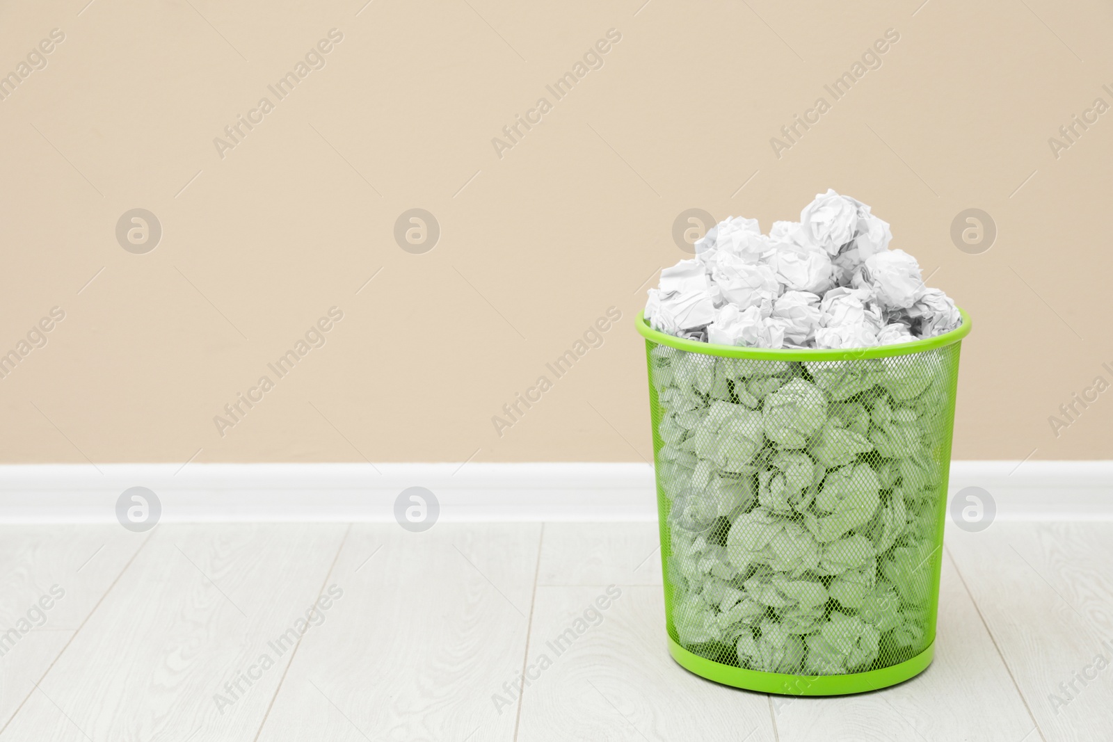 Photo of Metal bin with crumpled paper against color wall, space for text