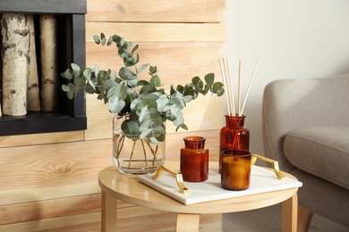Photo of Eucalyptus branches, aromatic reed air freshener and candles on wooden table in living room. Interior element