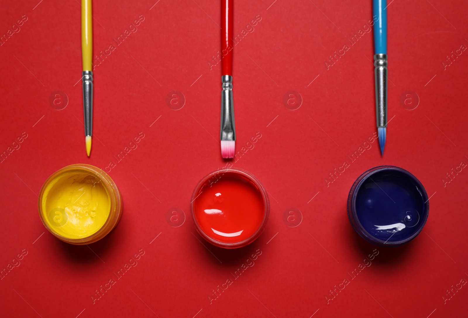 Photo of Brushes and jars with paint on red background, flat lay