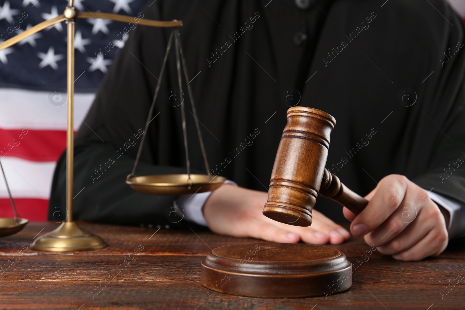 Photo of Judge with gavel at wooden table near flag of United States, closeup