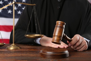 Photo of Judge with gavel at wooden table near flagUnited States, closeup