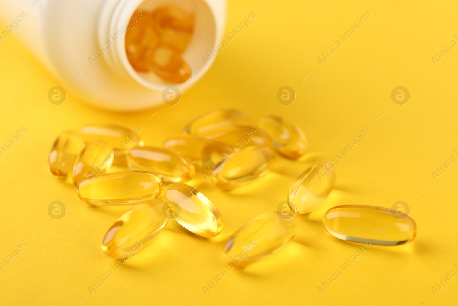 Photo of Vitamin capsules and medical bottle on yellow background, closeup