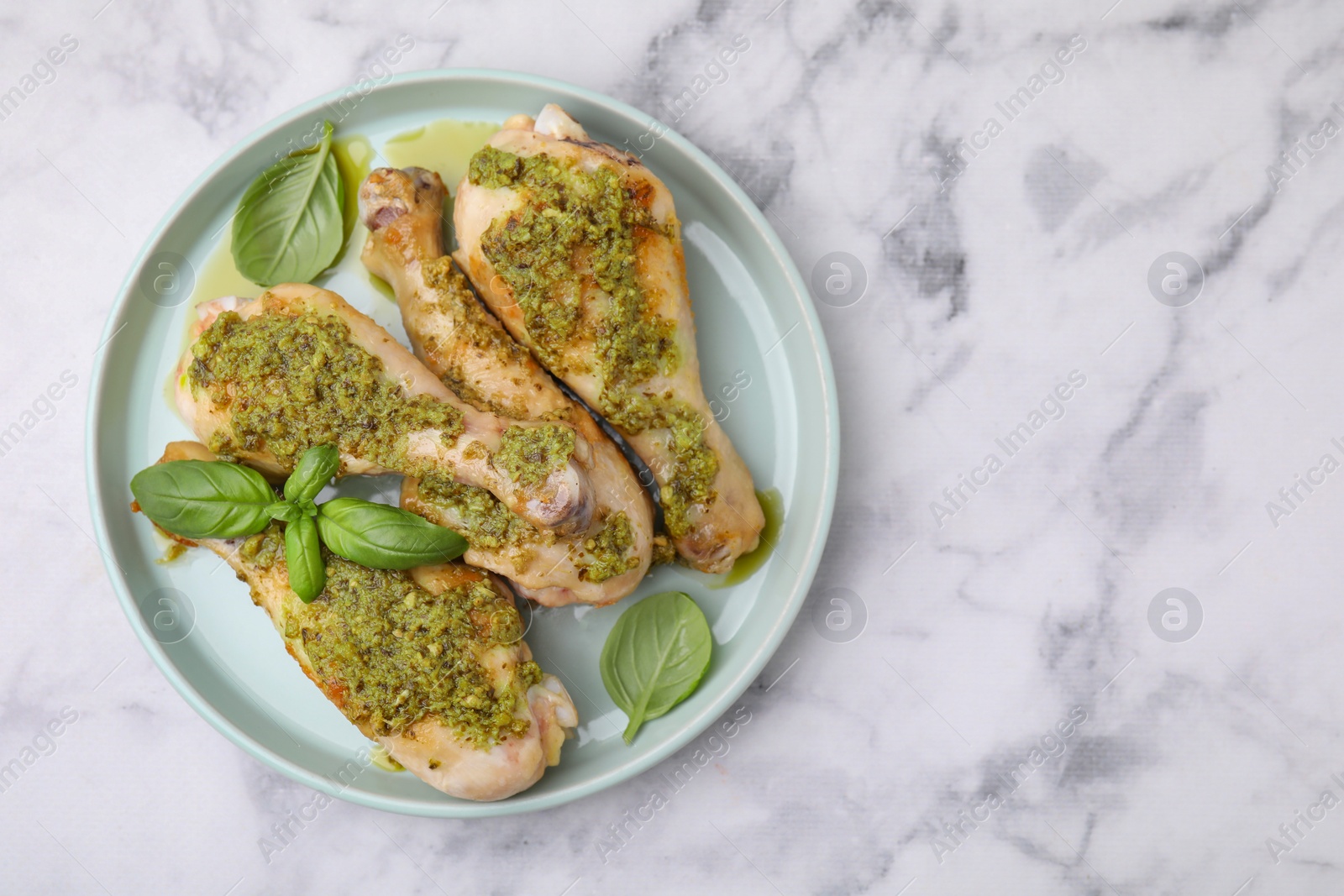 Photo of Delicious fried chicken drumsticks with pesto sauce and basil on white marble table, top view. Space for text