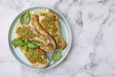 Photo of Delicious fried chicken drumsticks with pesto sauce and basil on white marble table, top view. Space for text