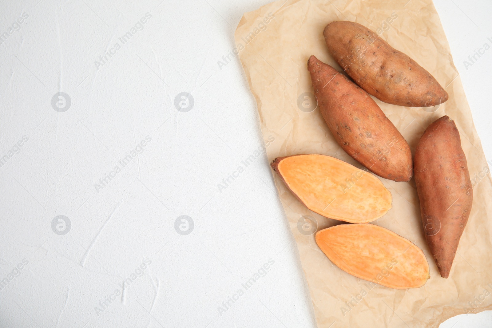 Photo of Parchment with cut and whole sweet potatoes on white table, top view. Space for text