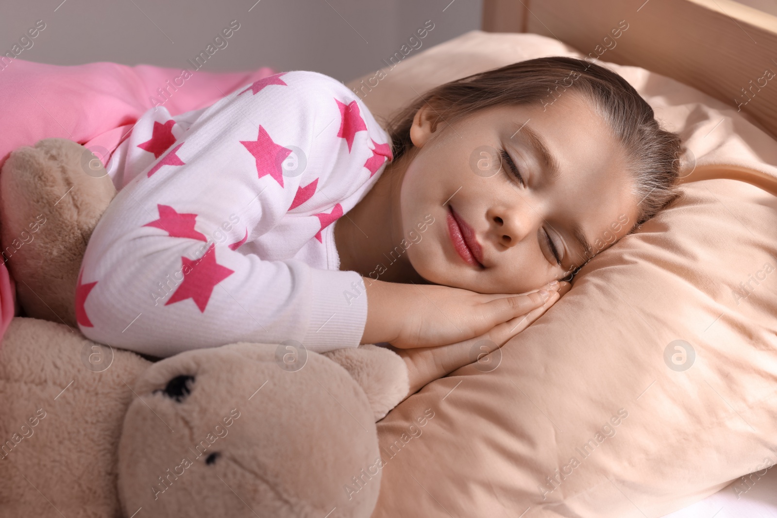 Photo of Cute little girl with toy bear sleeping in bed at home