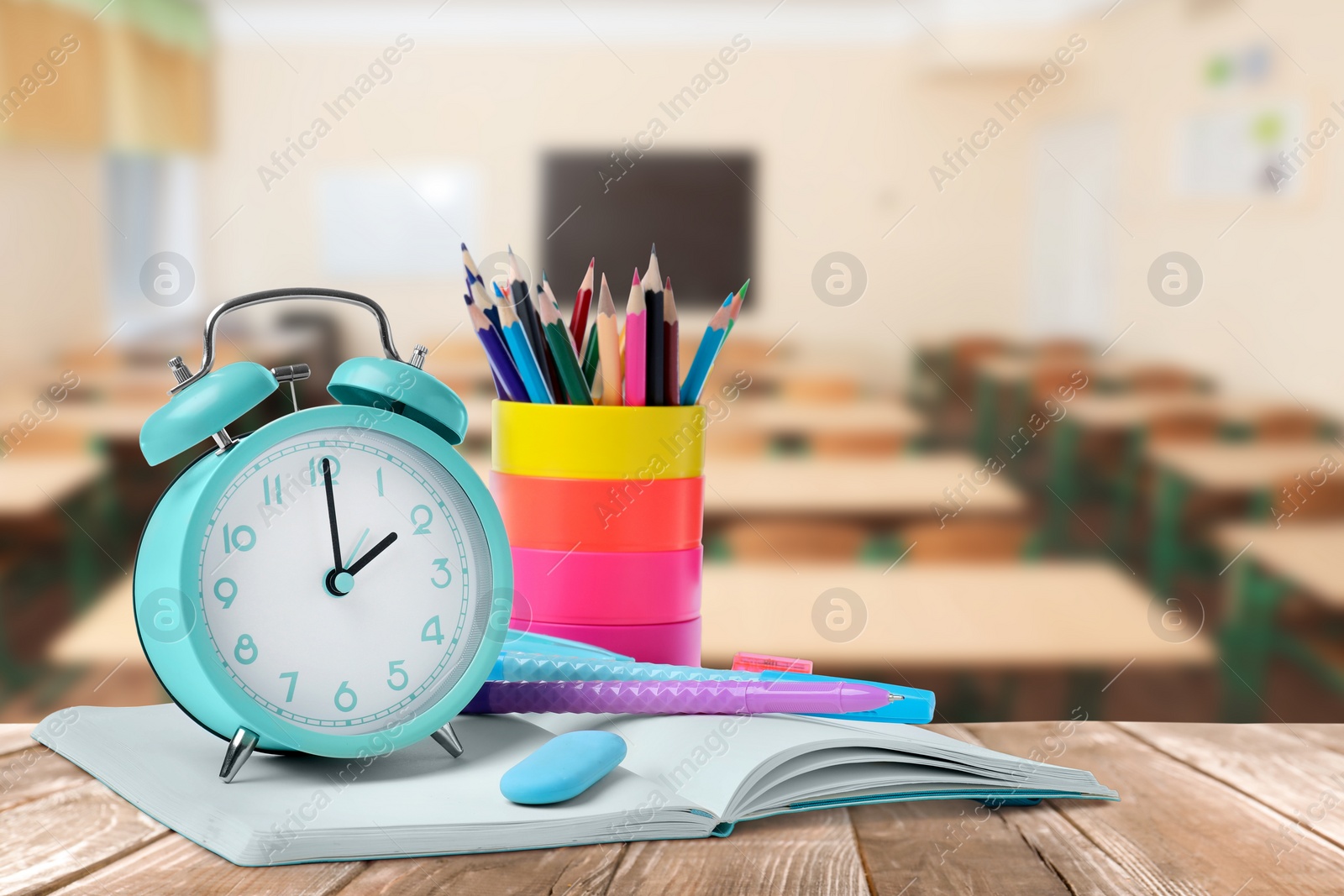 Image of Turquoise alarm clock and different stationery on wooden table in classroom