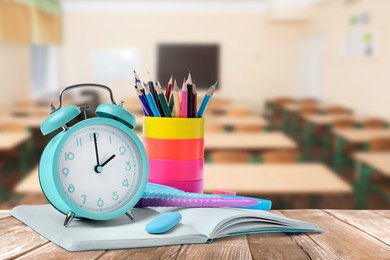 Turquoise alarm clock and different stationery on wooden table in classroom