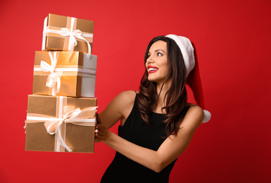 Photo of Beautiful woman wearing Santa hat with Christmas gifts on red background
