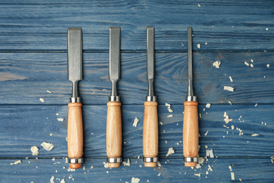 Photo of Modern chisels on blue wooden background, flat lay. Carpenter's tools