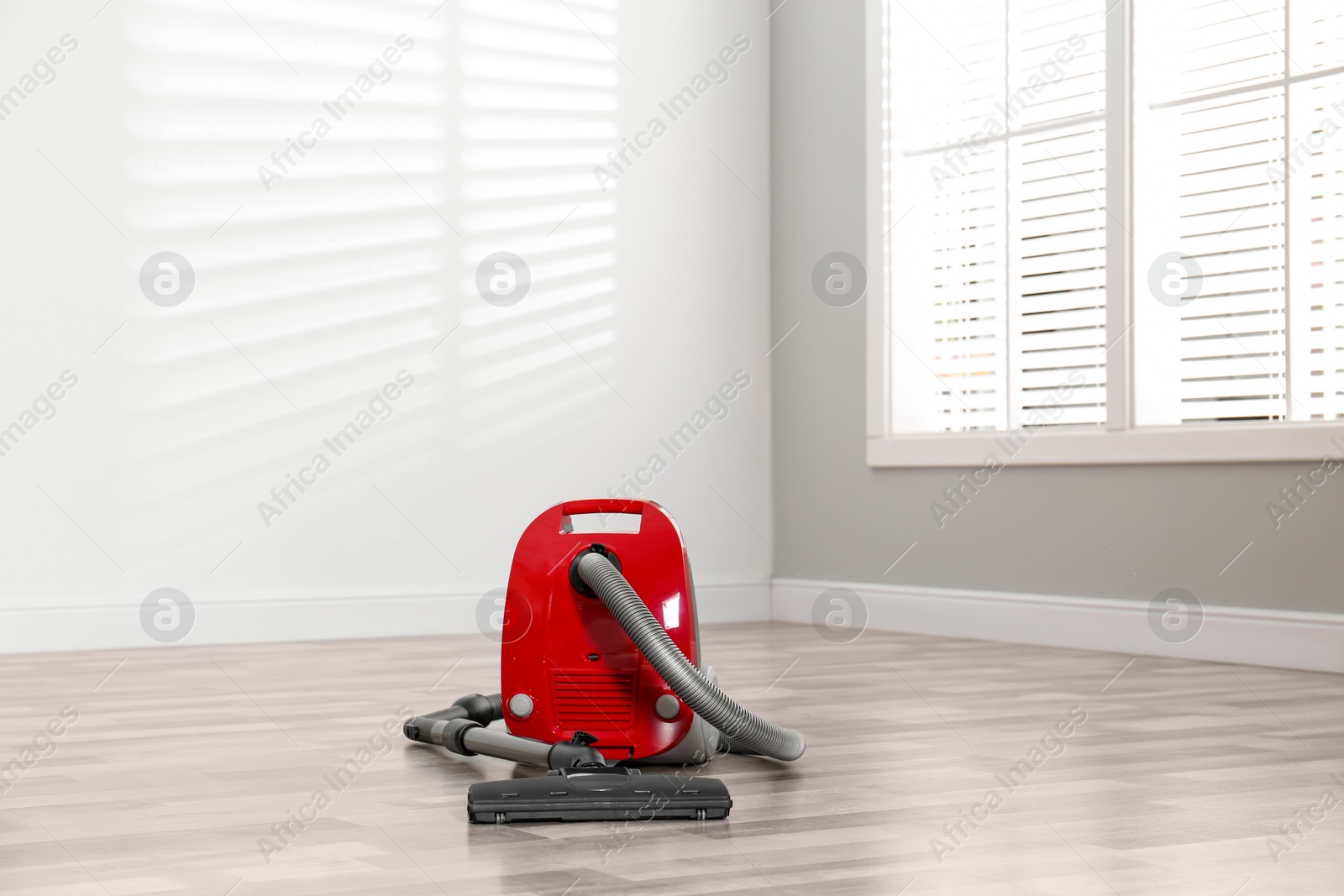 Photo of Modern red vacuum cleaner on floor indoors