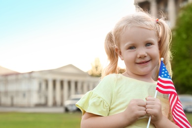 Photo of Cute little girl with American flag on city street. Space for text