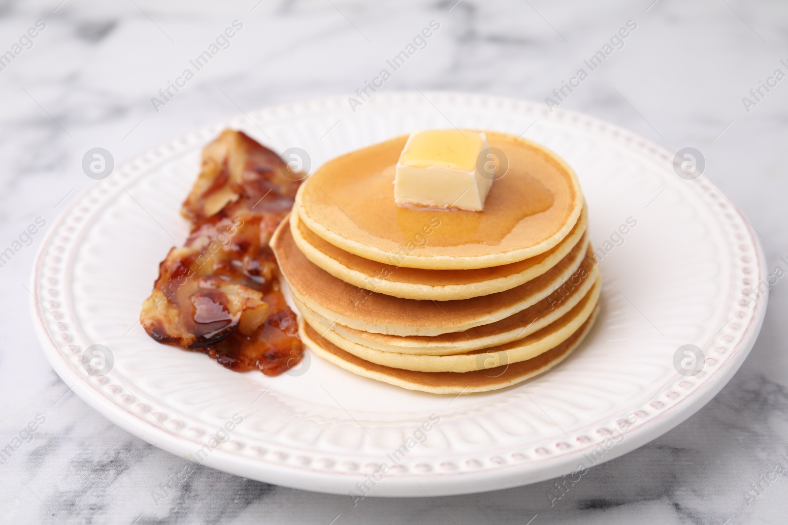 Photo of Delicious pancakes with butter, maple syrup and fried bacon on white marble table