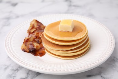 Photo of Delicious pancakes with butter, maple syrup and fried bacon on white marble table