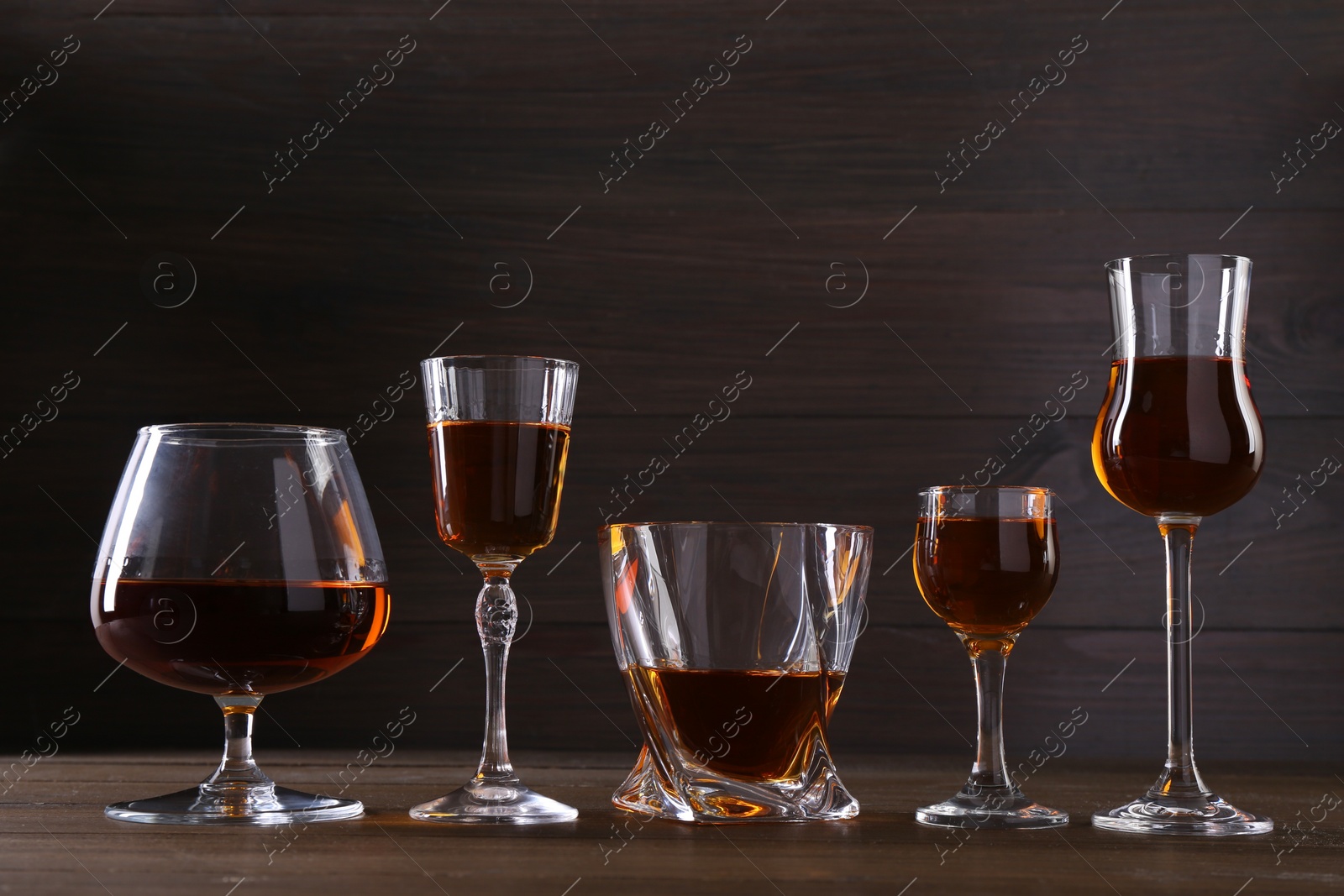 Photo of Different delicious liqueurs in glasses on wooden table