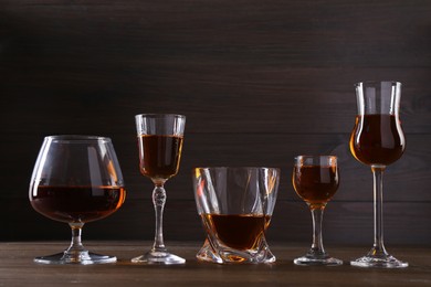 Different delicious liqueurs in glasses on wooden table