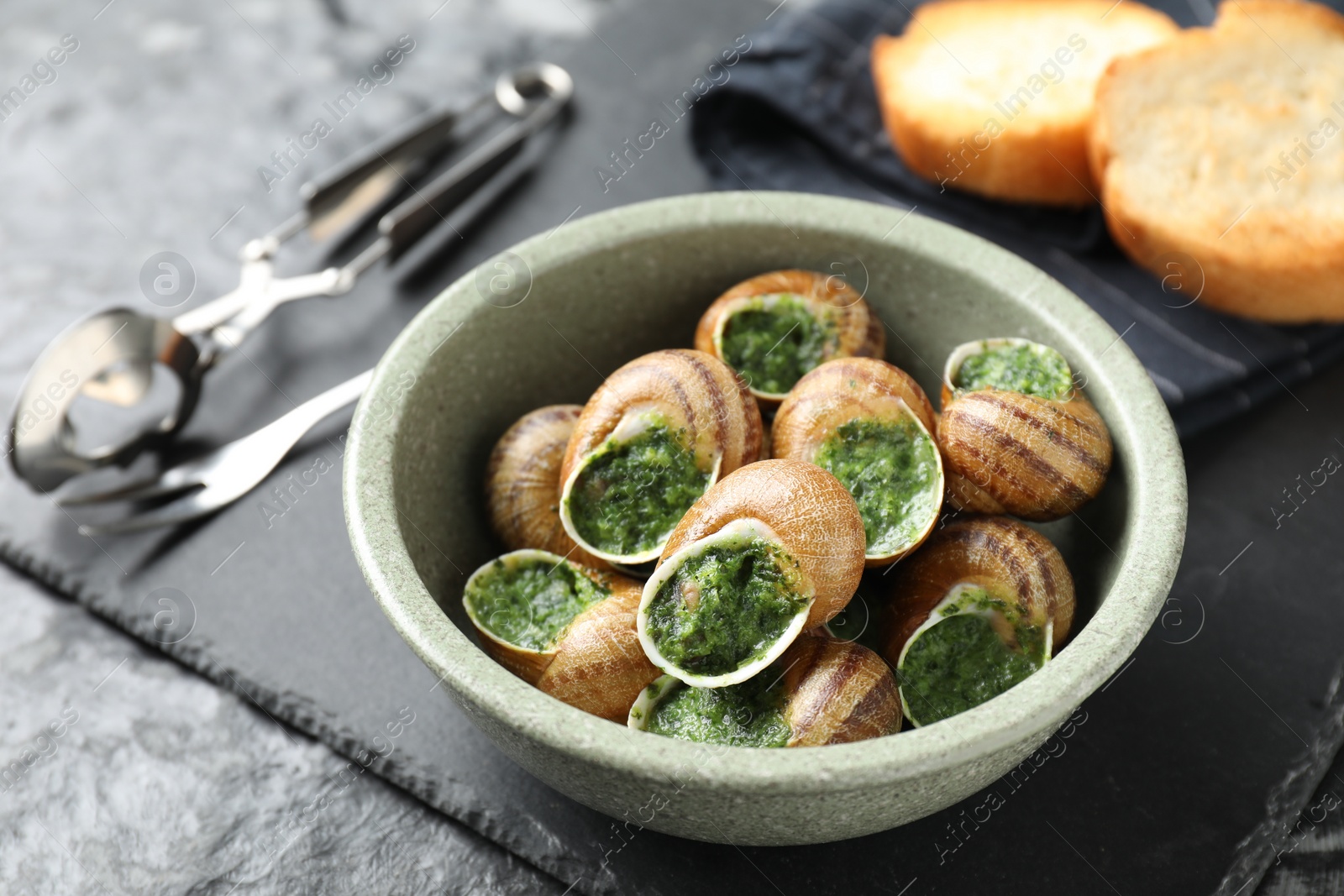 Photo of Delicious cooked snails served on grey textured table, closeup