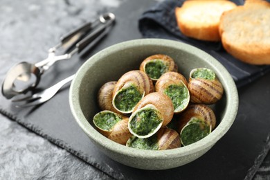 Photo of Delicious cooked snails served on grey textured table, closeup